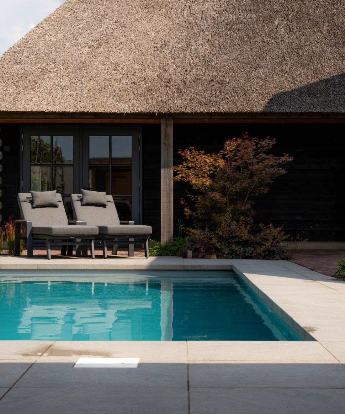 Luxe villa met rieten kap, twee grijze ligbedden en een langwerpig zwembad met helder blauw water