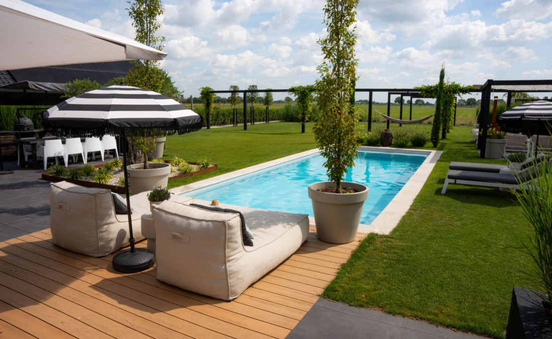 Helder blauw water in een rechthoekig zwembad in royale tuin omringd door gras en een terras met tafel en stoelen