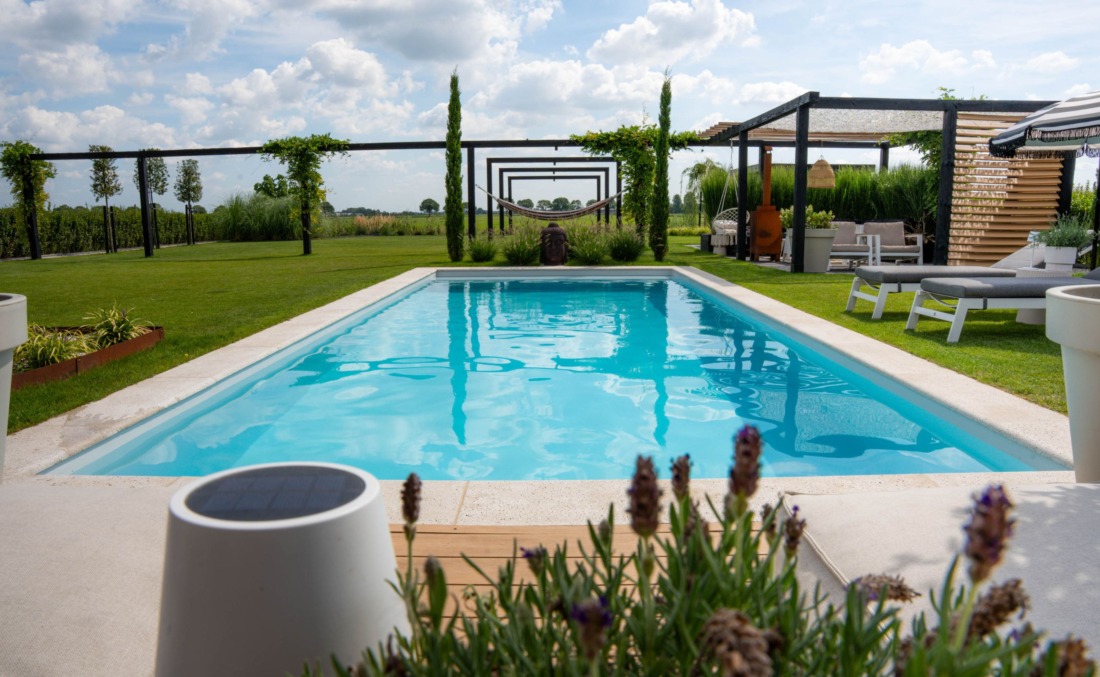 Grote tuin met langwerpig zwembad met helderblauw water in een tuin met verschillende zitgedeeltes