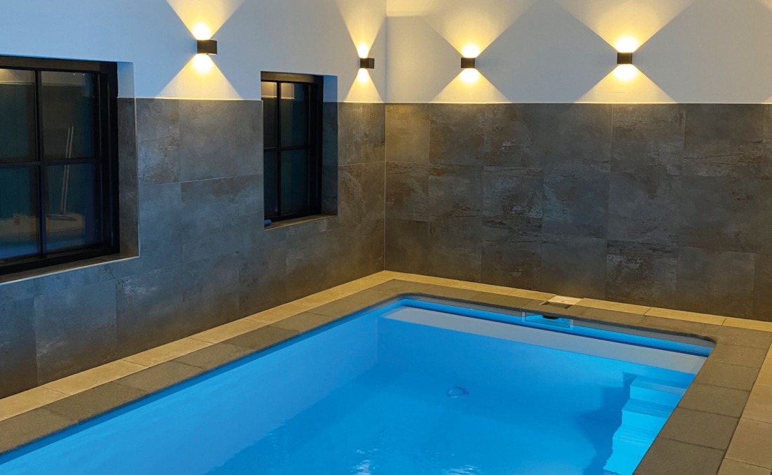 Binnenbad felblauw gekleurd water door de verlichting bij een grijze wand met lampjes