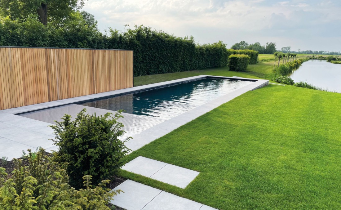 Langwerpig buitenzwembad met lamellen zwembadafdekking in de kleur grijs/zilver in royale tuin