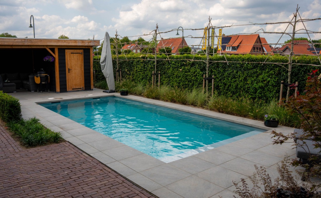 Langwerpig skimmerzwembad met houten schuurtje, een BBQ en een parasol met hoes eromheen