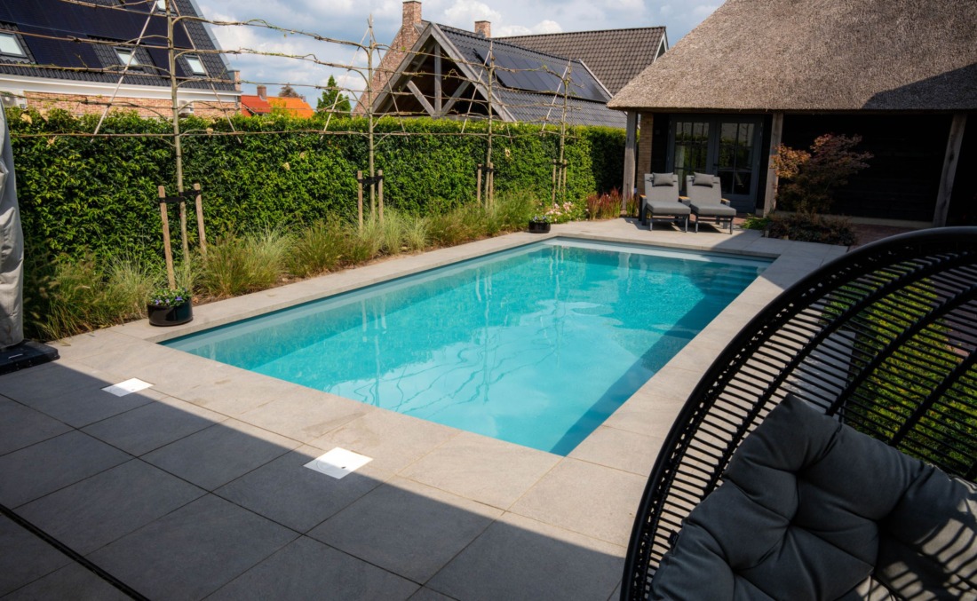Luxe tuin met rechthoekig zwembad, twee grijze ligbedden en een hangstoel