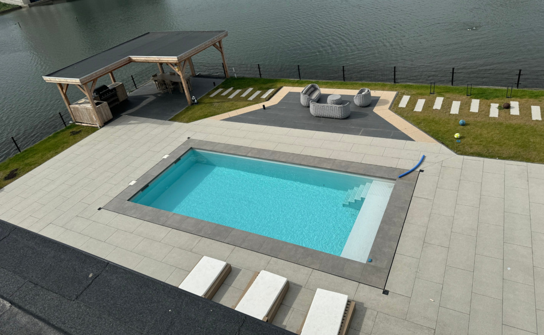 Lichtblauw HDPE maatwerk zwembad van JDL met brede inlooptrap, gelegen in een luxe tuin direct aan het water.