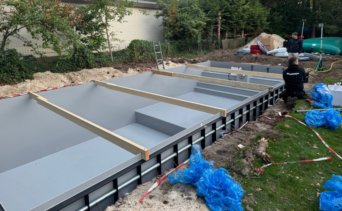 Monteurs van JDL bezig met de installatie van een grijs HDPE zwembad, waarbij de externe ribbenconstructie en houten stempels goed zichtbaar zijn.