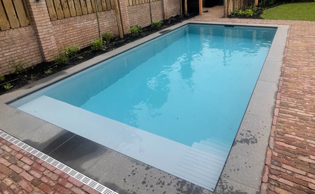 Strak JDL kunststof zwembad met grijze randtegels, naadloos aangesloten op een terras van authentieke gebakken klinkers.