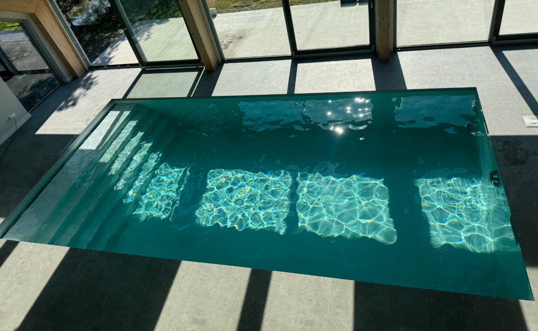 Strak binnenzwembad van JDL in een ruimte met grote glaspartijen, waardoor het zonlicht mooi reflecteert op het water.
