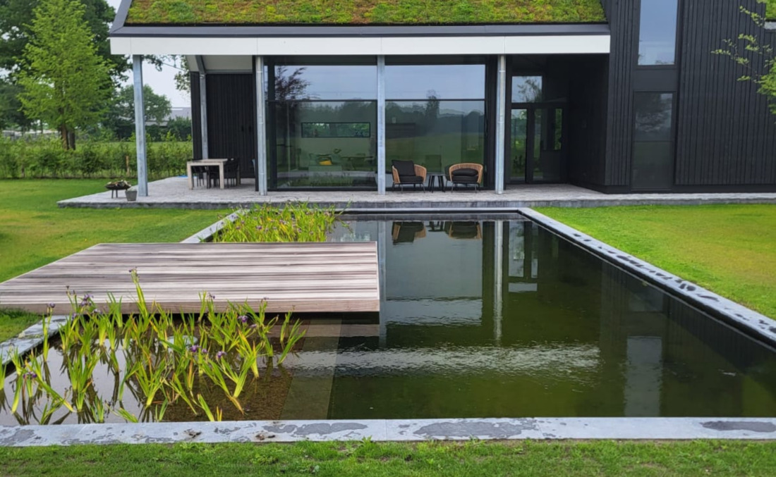 Exclusieve strakke zwemvijver van JDL bij een moderne villa met zwart hout en sedumdak, voorzien van een stijlvolle vlonderbrug.