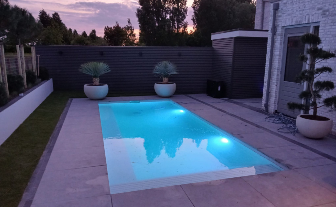 Luxe wit HDPE zwembad van JDL met ingebouwde LED-verlichting, sfeervol verlicht tijdens de avondschemering in een moderne tuin.