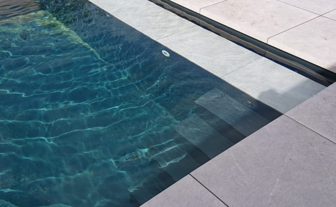 Diepblauw ogend water in een donkere zwembadkuip, met zicht op de strakke afwerking van de hoektrap en plage.
