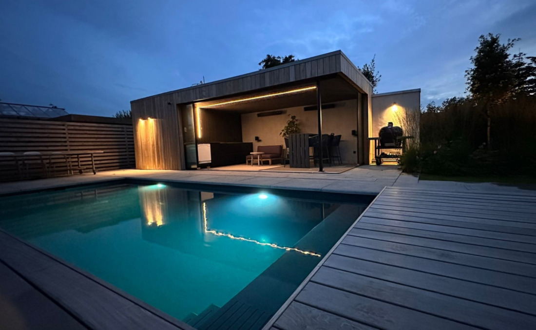 Sfeervol verlicht JDL zwembad in de avondschemering, gelegen naast een luxe houten poolhouse met buitenbar en warme accentverlichting.